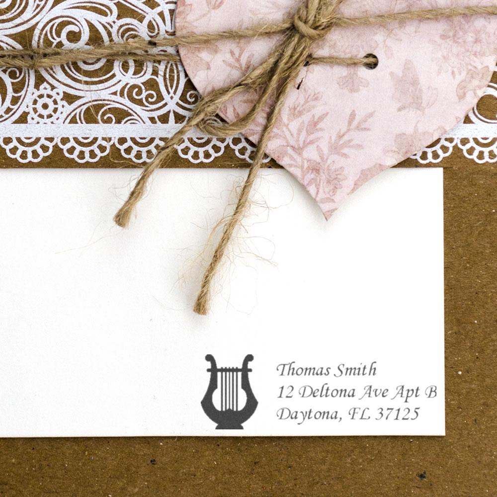 Custom return address rubber stamp with lyre icon on a kraft wedding invitation envelope.