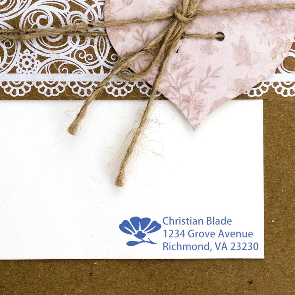 Custom return address rubber stamp on a white envelope with floral gift wrap and twine accents.