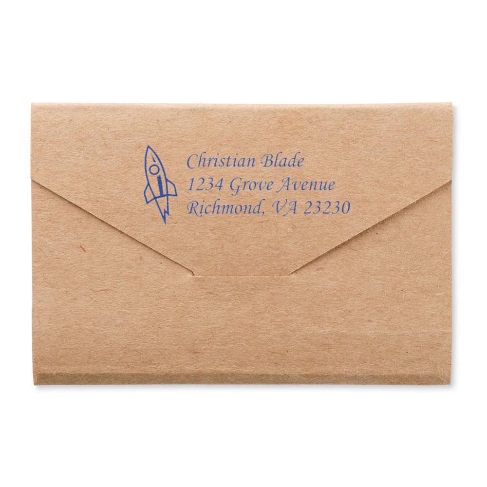 Custom return address rubber stamp with rocket icon on kraft envelope, showing blue address imprint for mailing.