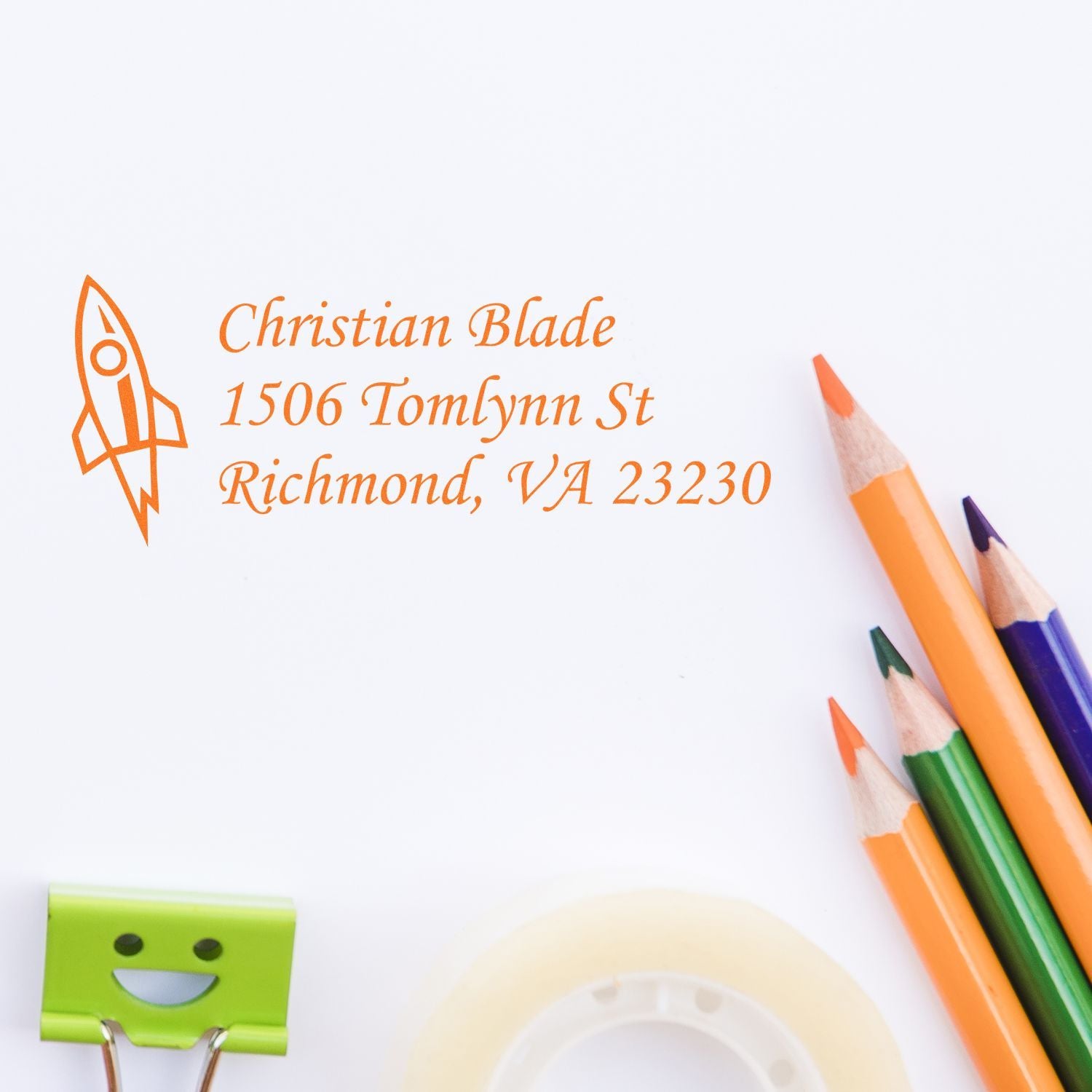 Personalized rubber address stamp with rocket logo for Christian Blade, Richmond VA 23230, shown beside colored pencils.