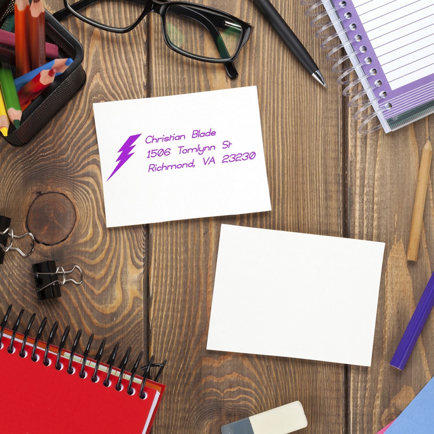 Custom purple return address rubber stamp on stationery with lightning logo, shown on a desk with office supplies.