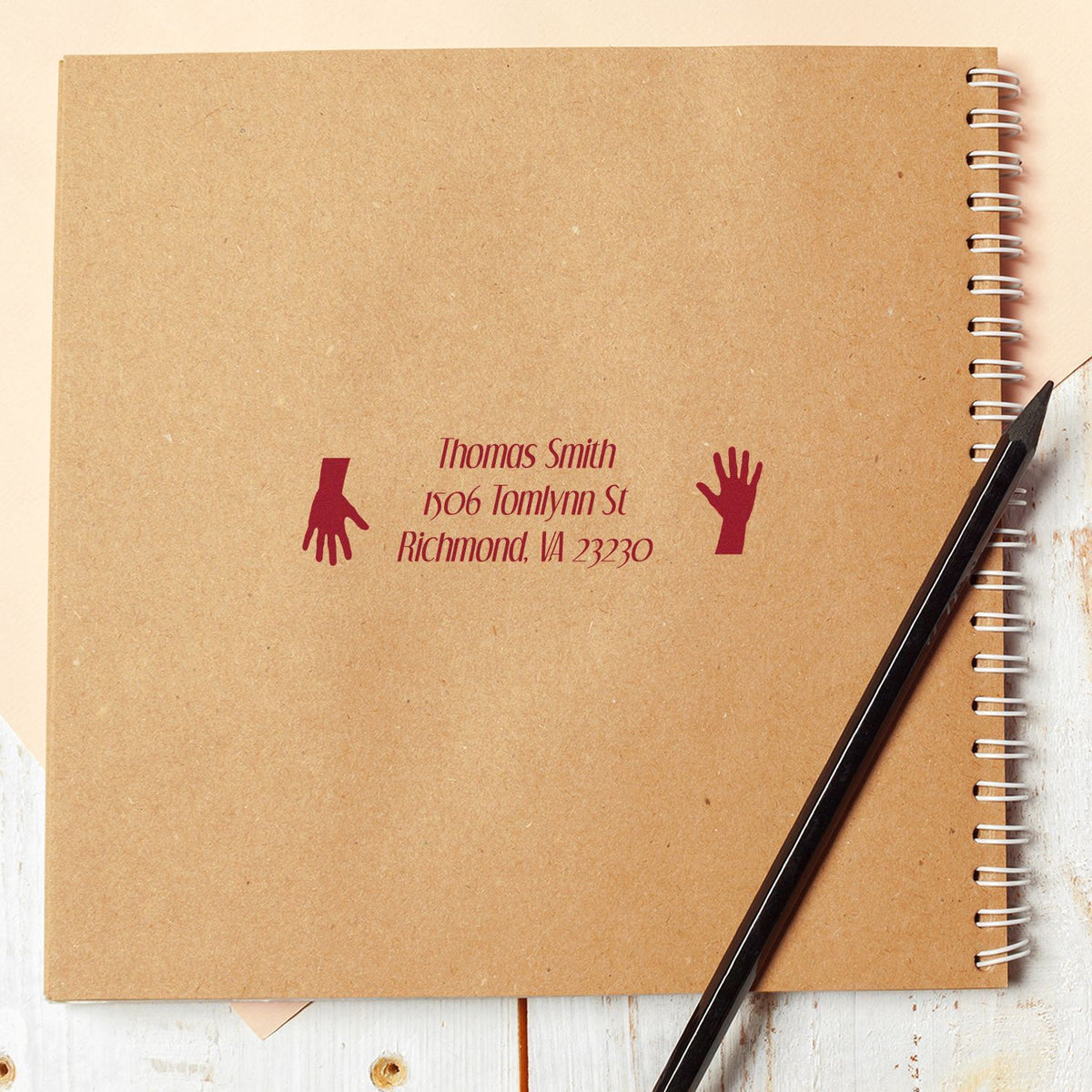 Custom return address rubber stamp on kraft notebook cover, with hands design for personalized stationery branding.