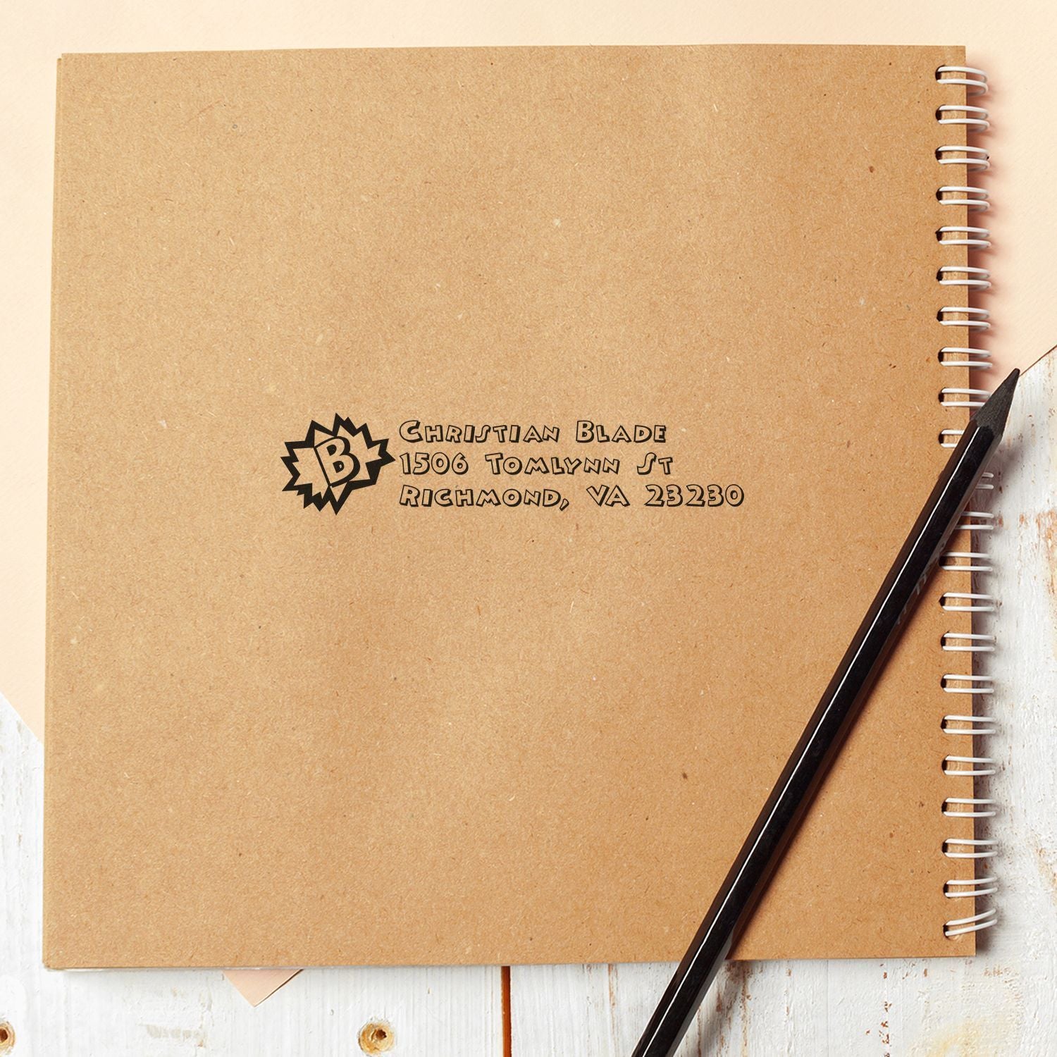 Custom return address rubber stamp imprint on kraft notebook cover with logo, business name, and address.
