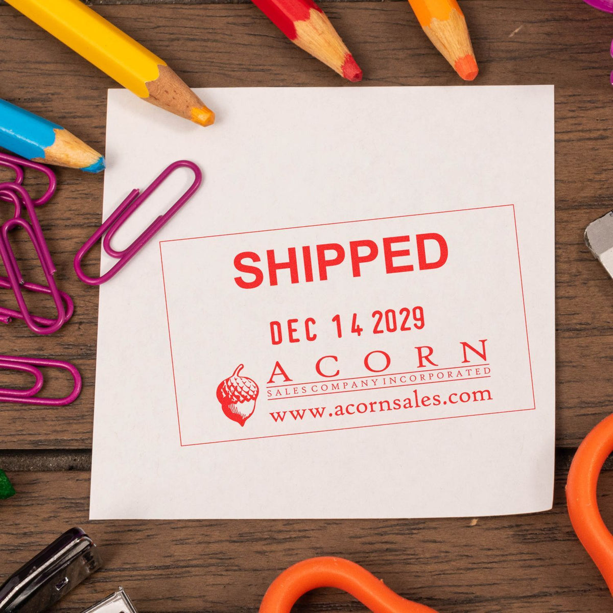Shipped stamp on white paper with colorful pencils and paper clips on a wooden desk, featuring Acorn Sales branding.