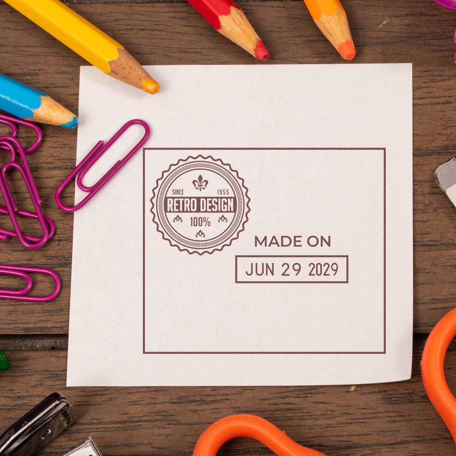 Blank paper with retro design stamp, made on Jun 29 2029, surrounded by colorful pencils and paper clips on a wooden desk.
