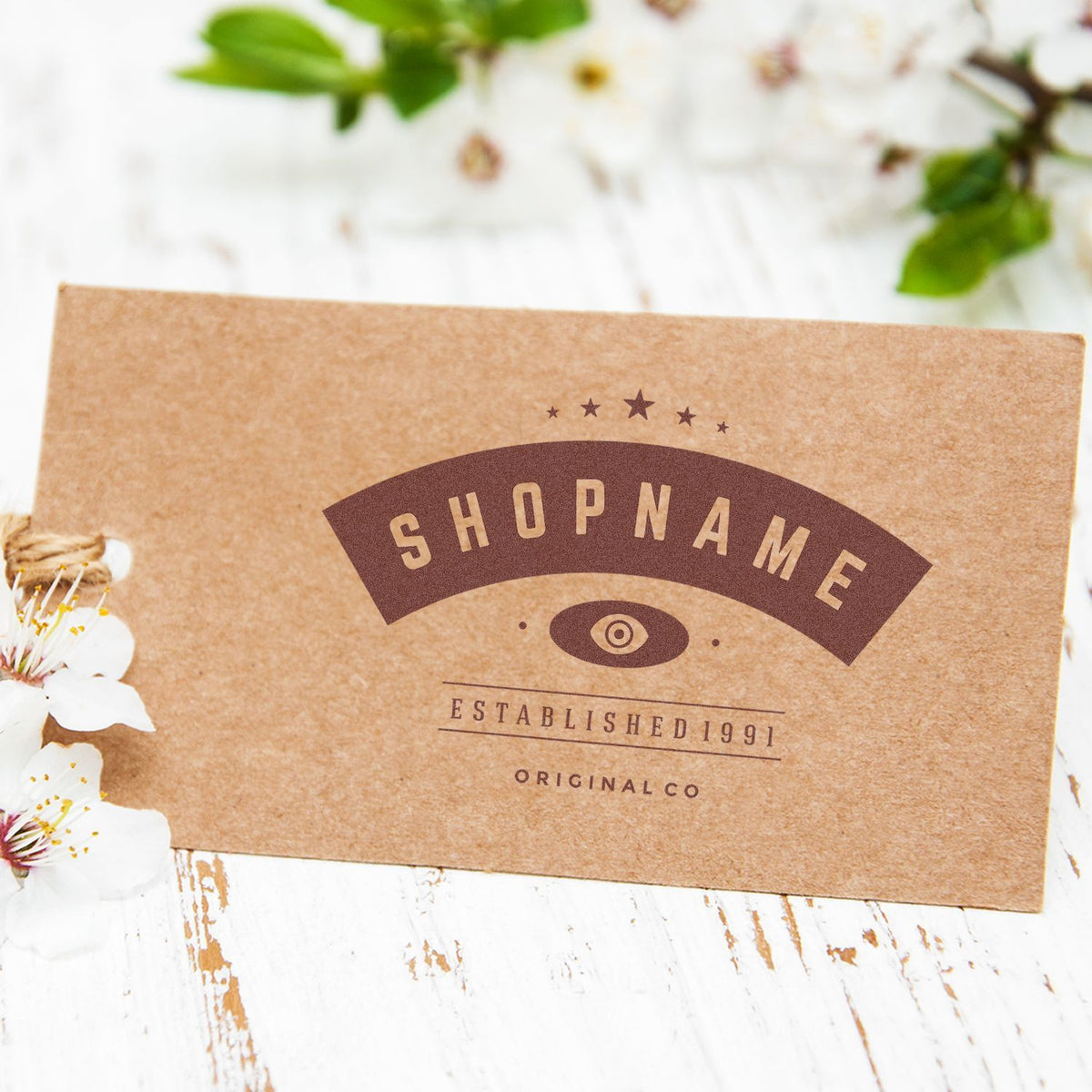Shopname brand kraft packaging label reading Established 1991 Original Co on rustic white background with spring flowers
