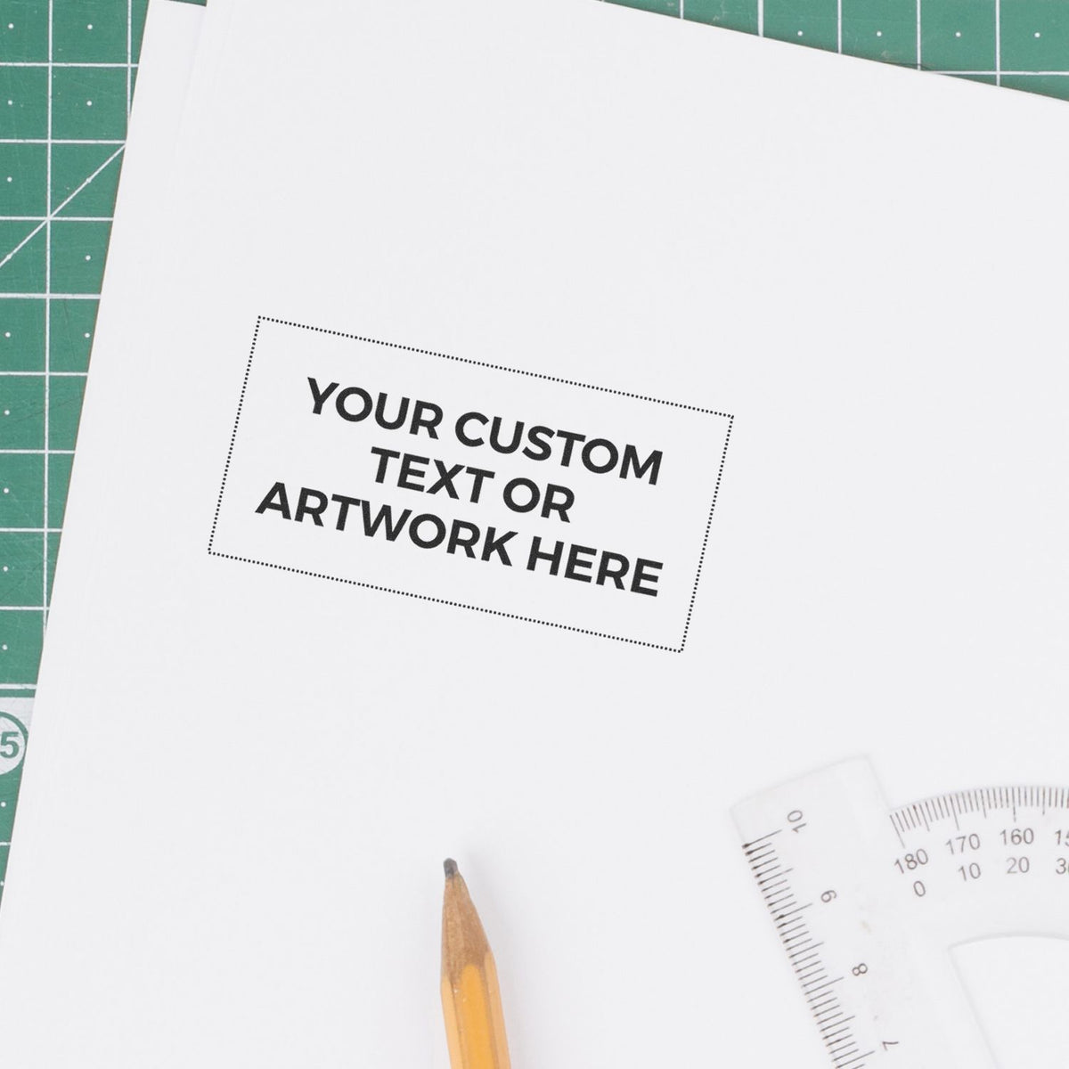 Blank custom text or artwork mockup on white paper with pencil, protractor, and cutting mat for graphic design template.