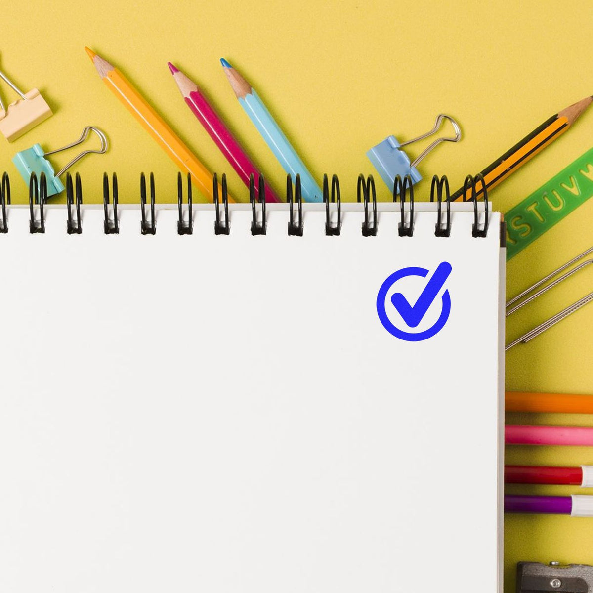 Color pencils and lined notebook with checkmark icon, representing organized school notes, planning, and homework readiness.