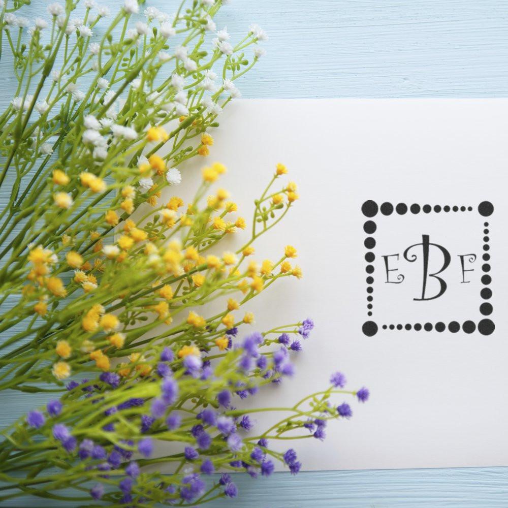 Custom monogram rubber stamp sample on white card with floral sprigs, ideal for personalized stationery.