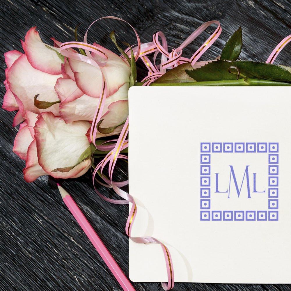 Custom monogram rubber stamp on wedding stationery with pink roses and ribbon for personalized invitation branding.