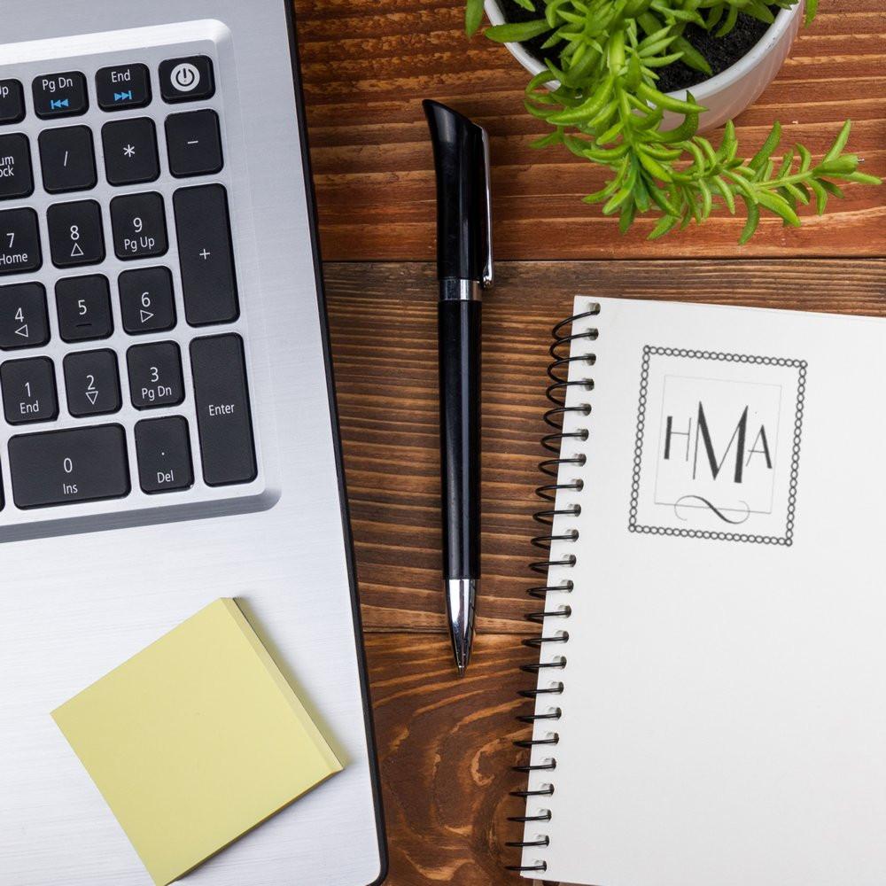 Custom monogram rubber stamp impression on spiral notebook beside laptop and pen for branded stationery.