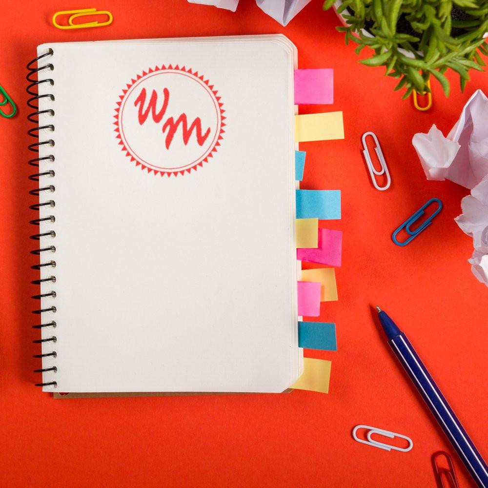 Custom rubber stamp monogram on spiral notebook with colorful tabs, ideal for planner organization, office branding, and stationery.