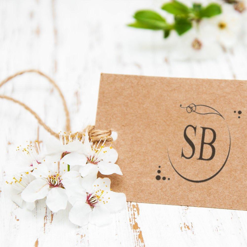 Custom monogram rubber stamp with SB initials on a kraft gift tag, tied with twine and white flowers.