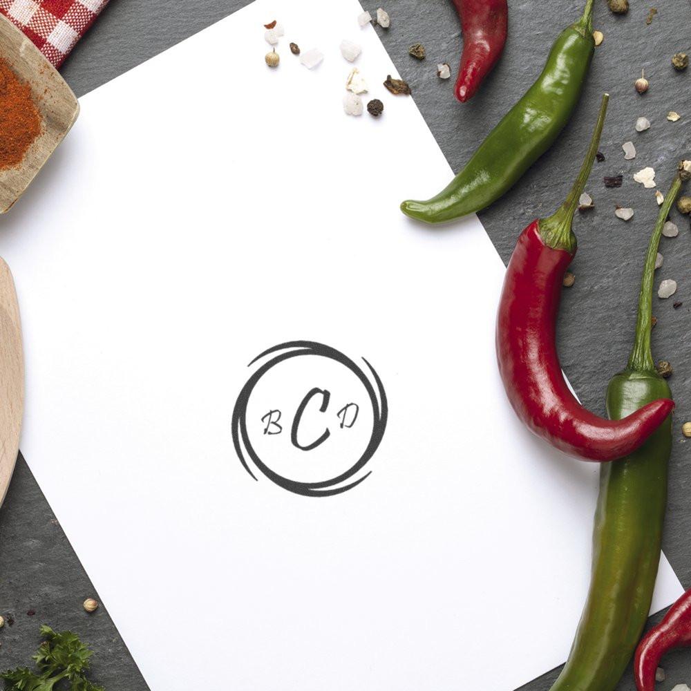 Custom monogram rubber stamp logo on blank paper with chili peppers and spices for culinary branding.