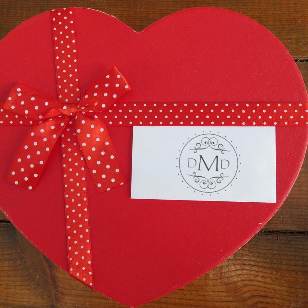 Custom rubber stamp logo card on heart-shaped gift box with red polka dot ribbon, ideal for personalized gift packaging.