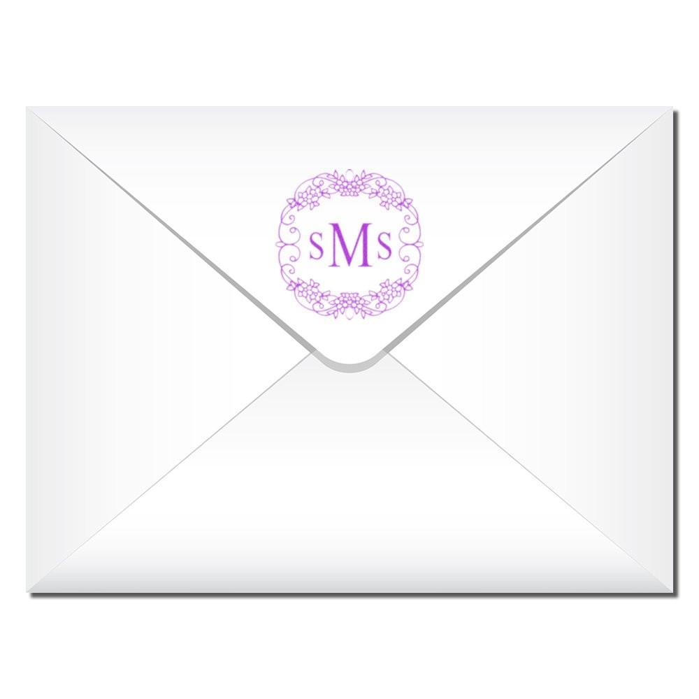 Custom monogram rubber stamp for envelopes, featuring a purple floral wreath logo on a white invitation envelope.