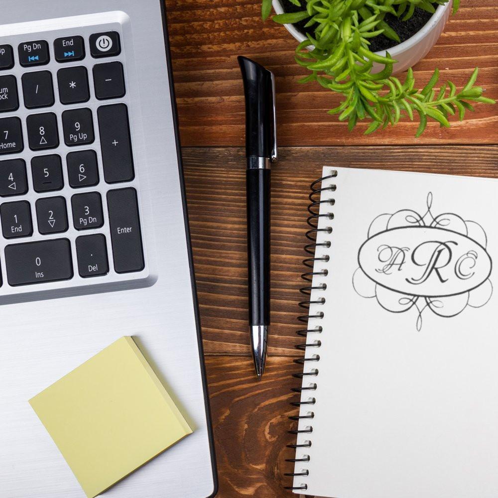 Custom monogram rubber stamp on a notebook beside a laptop and pen, ideal for personalized office branding and stationery.