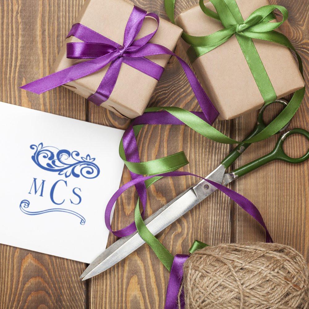 Gift wrapping supplies with monogram card, purple and green ribbons, scissors and twine on wooden background for holiday DIY presents