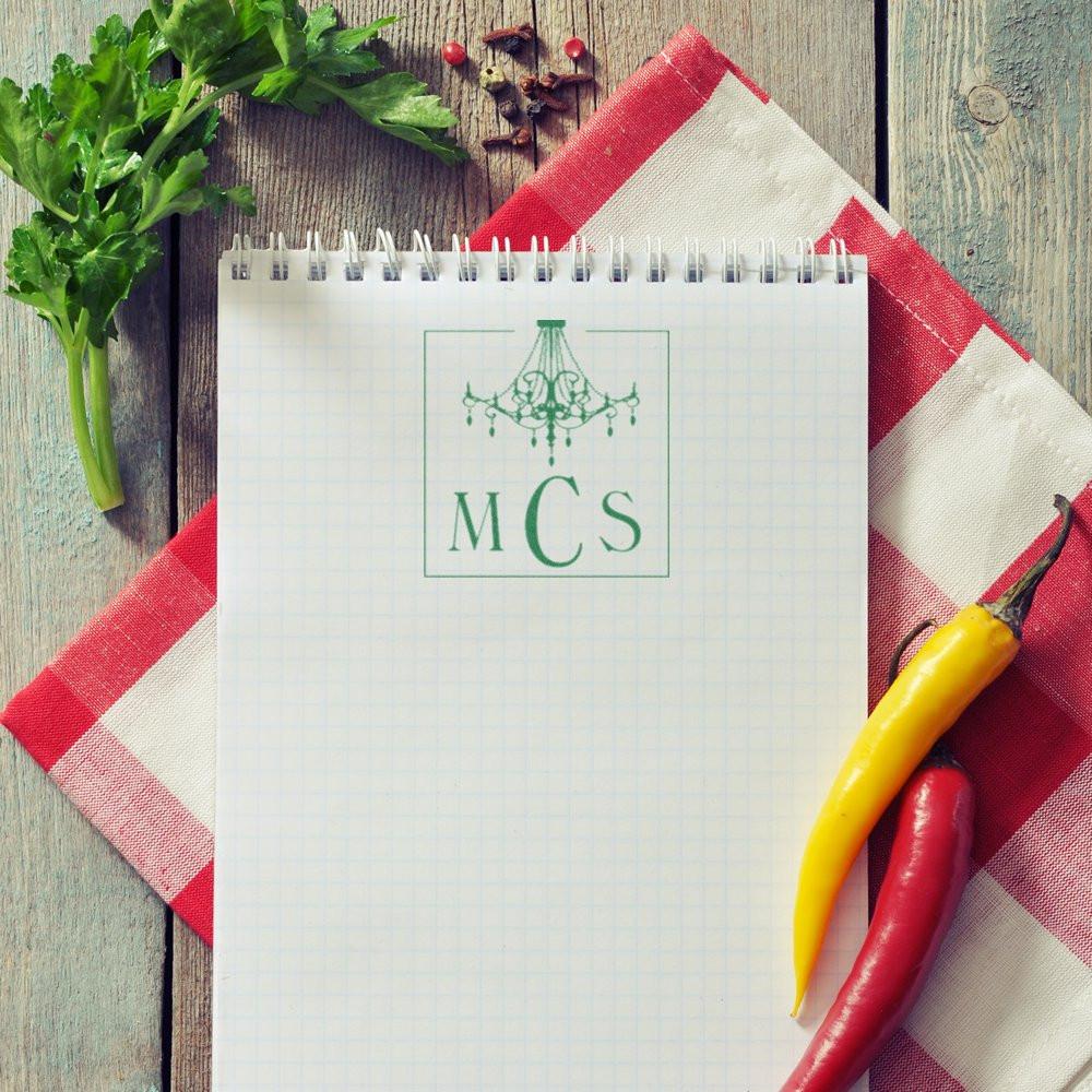 Recipe notebook with monogram MCS, parsley, and chili peppers on striped cloth for food prep and cooking notes.