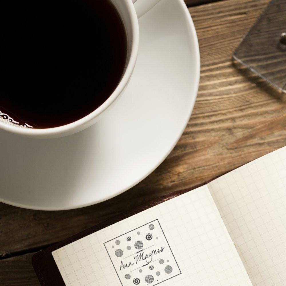 Custom rubber stamp impression in notebook beside a cup of coffee on a rustic wooden desk.