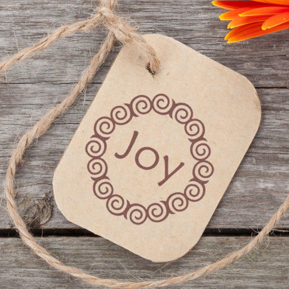 Joy rubber stamp style on kraft gift tag with twine, perfect for handmade packaging, holiday crafts, and rustic gift wrapping.