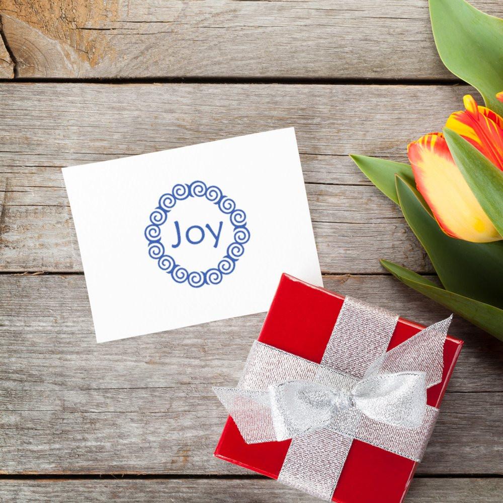 Joy rubber stamp on a greeting card beside a wrapped gift box and tulips, ideal for holiday card making.