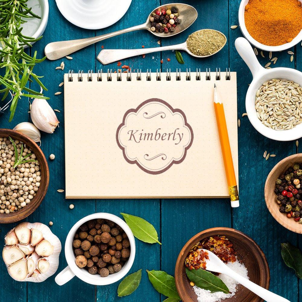 Personalized rubber stamp mockup with Kimberly name stamp on notebook, surrounded by kitchen spices and ingredients