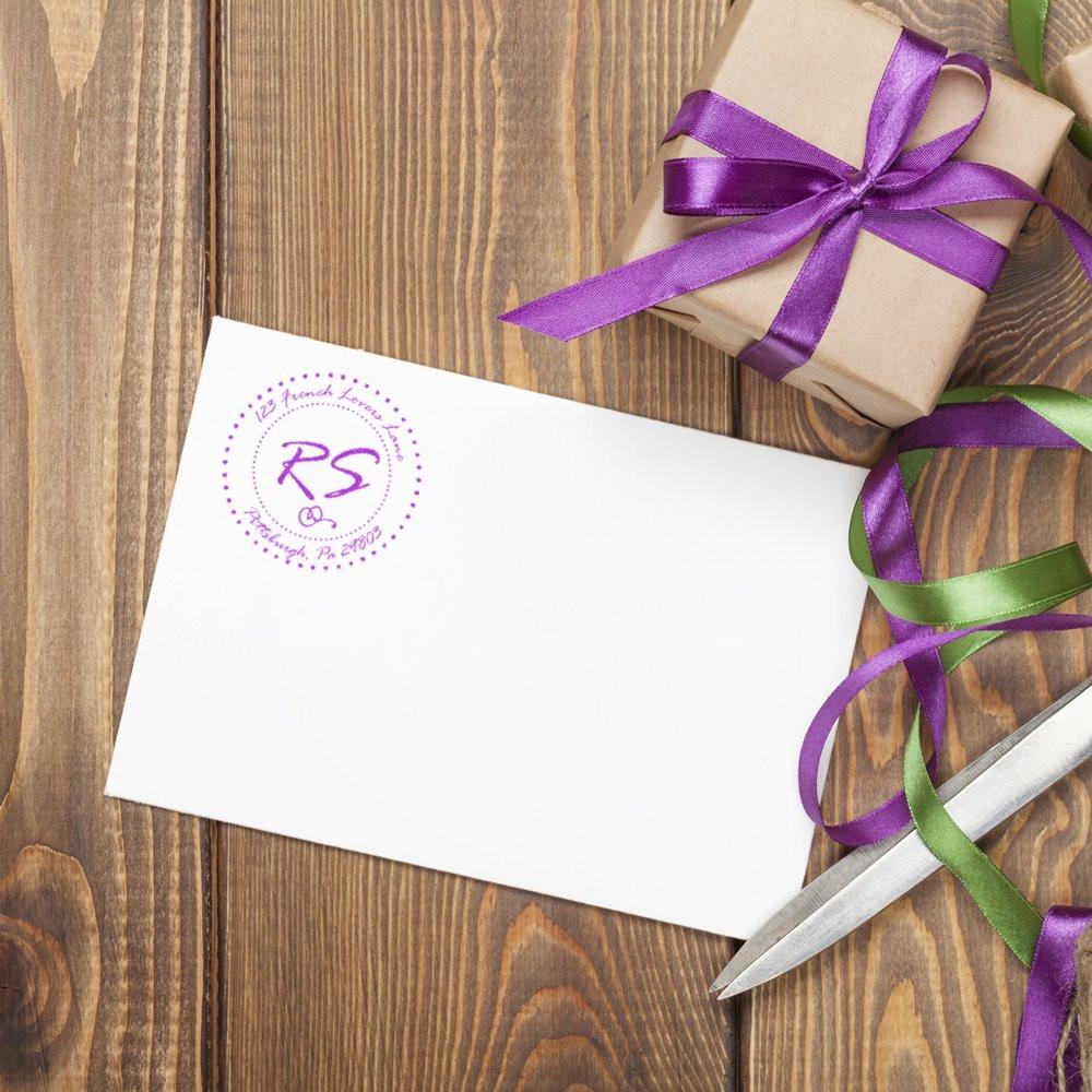 Custom purple return address rubber stamp on white envelope beside gift wrap ribbon and scissors, ideal for personalized mailings.