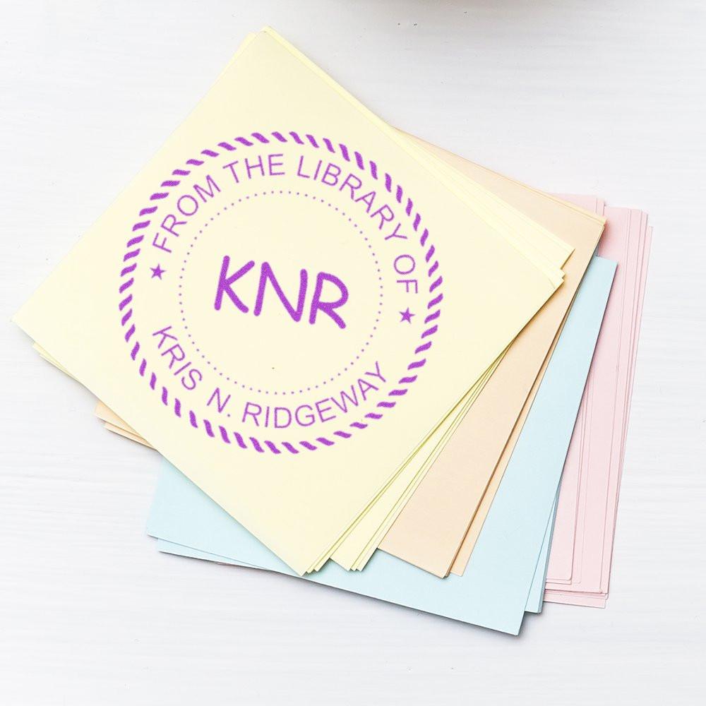 Personalized library rubber stamp impression on pastel paper stack reading From the Library of Kris N. Ridgeway
