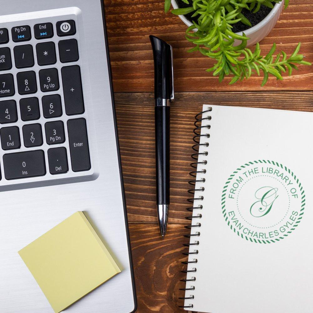 Custom library rubber stamp bookplate on a notebook beside a laptop, pen, and desk plant for personalized book branding.