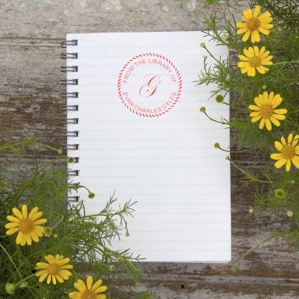 Personalized library rubber stamp on a spiral notebook, showing a custom From the Library Of book ownership design.