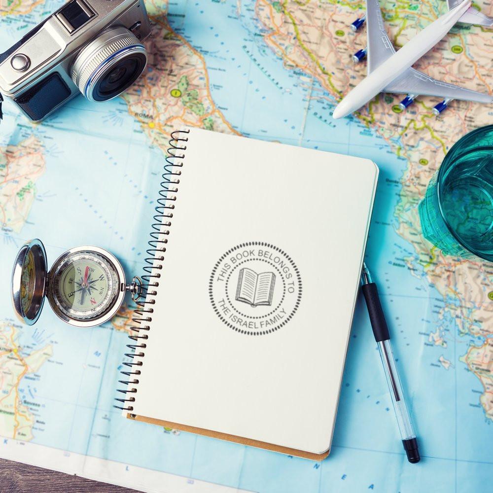 Custom rubber book stamp on a notebook over a world map, with travel accessories for personalized journaling.