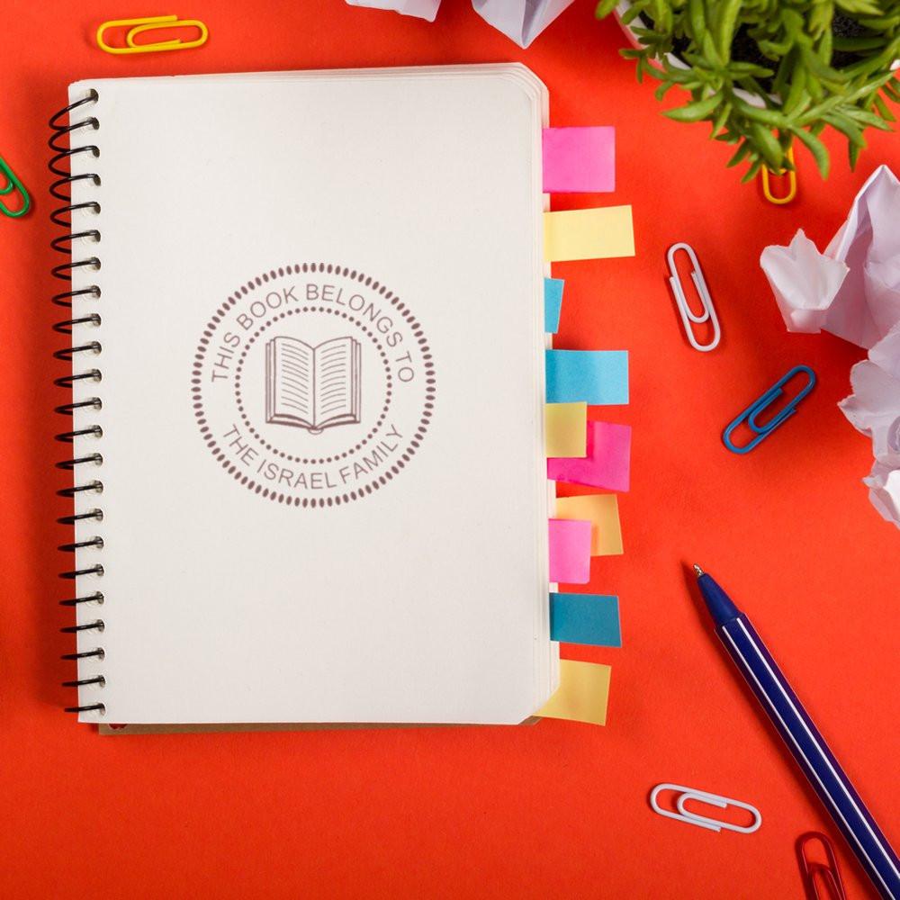 Custom rubber book stamp on notebook reading This Book Belongs to the Israel Family for personalized library ownership.