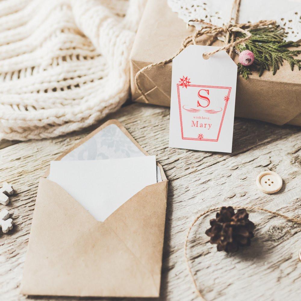 Holiday Christmas greeting card with gift tag reading Mary, with love on rustic wood beside envelope, pine branches and pinecone.