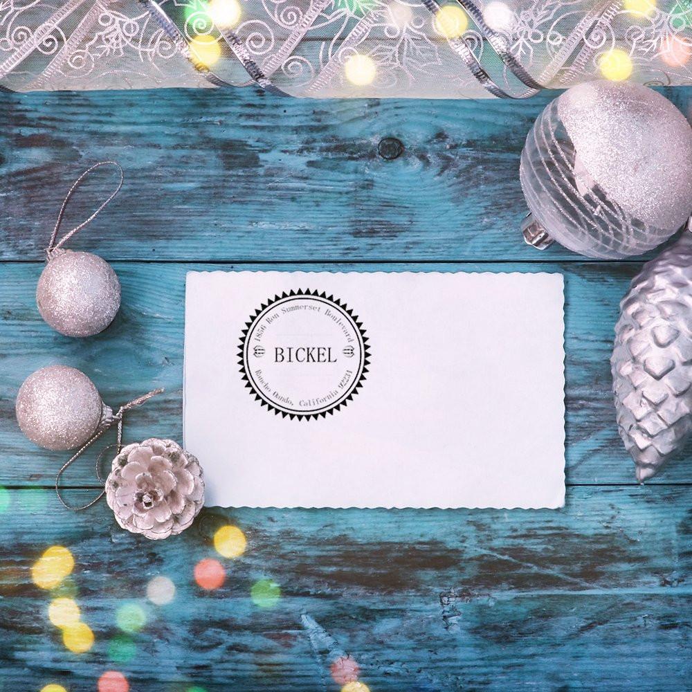 Personalized return address rubber stamp on a white card with festive silver ornaments on a blue wood background.