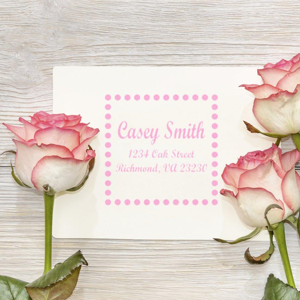 Custom address rubber stamp impression in pink, personalized with name and return address, framed by roses on white card.