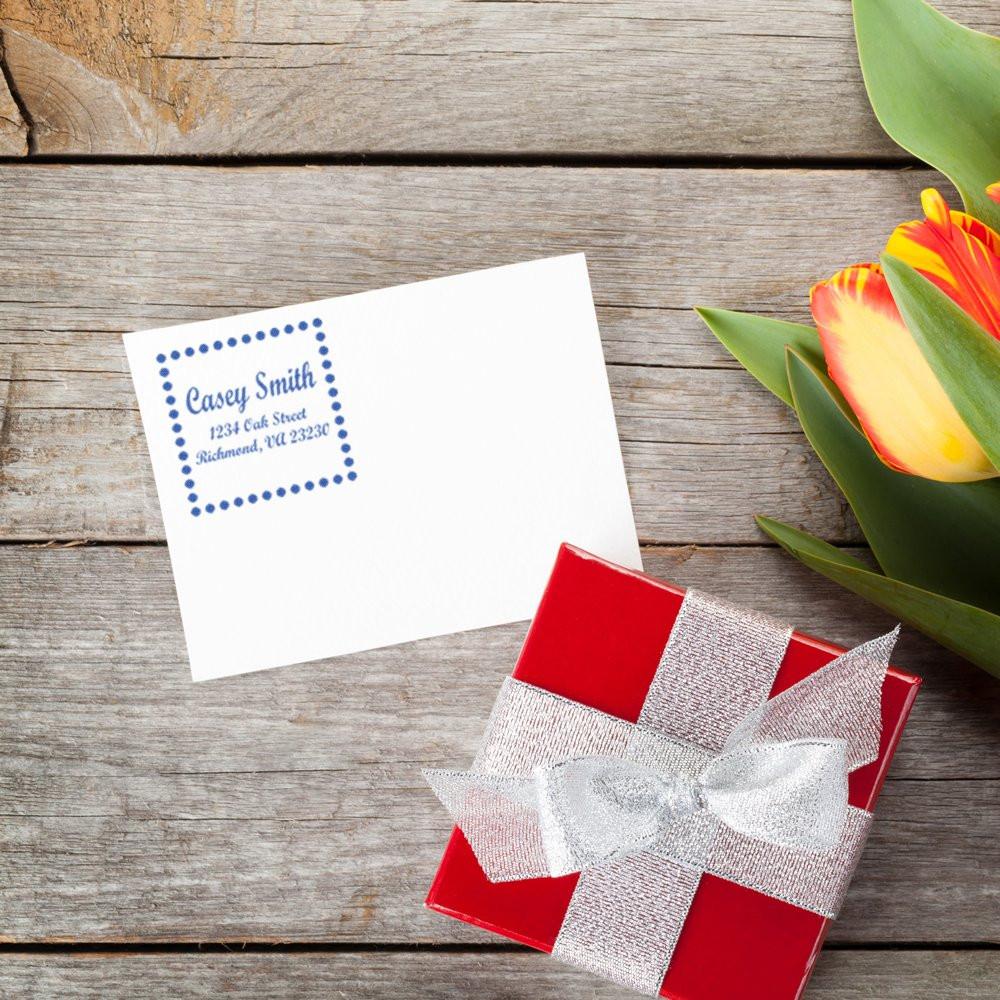 Personalized address rubber stamp on envelope, paired with gift box and flowers for wedding stationery or mailing.