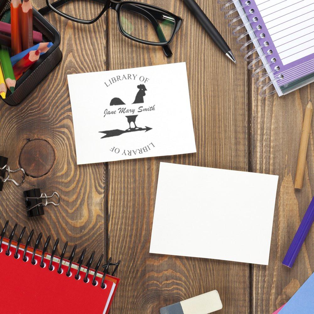 Personalized library rubber stamp impression on paper beside stationery, showing a custom book ownership stamp.