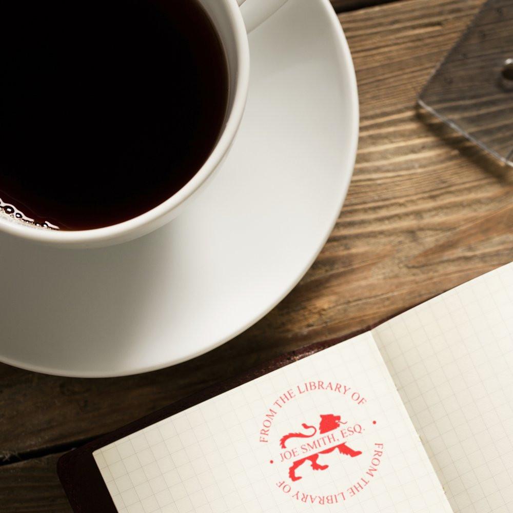 Personalized library rubber stamp imprint in a notebook beside coffee, ideal for custom bookplate and journal branding.