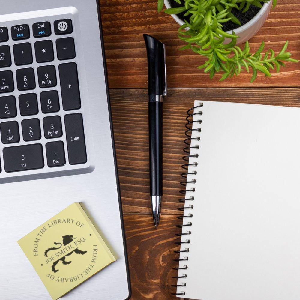 Custom library rubber stamp on desk with laptop, notebook and pen, perfect for personalized bookplate and office branding.