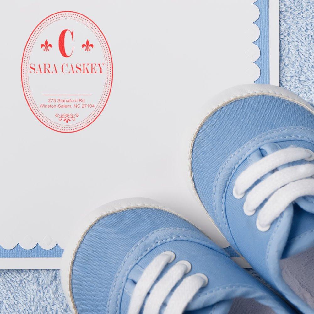 Custom monogram rubber stamp for baby shower invitations and thank-you cards, shown on stationery with blue baby shoes.