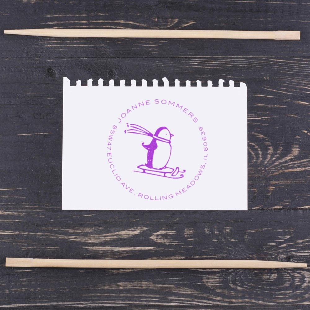 Custom rubber stamp impression with penguin logo and circular address text, shown with wooden handles for branding.