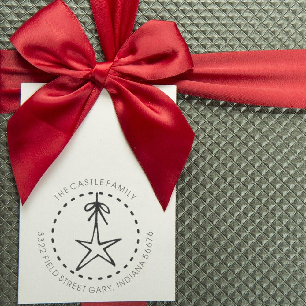 Custom return address rubber stamp on a gift tag with red bow, featuring a family name, address, and star ornament logo.