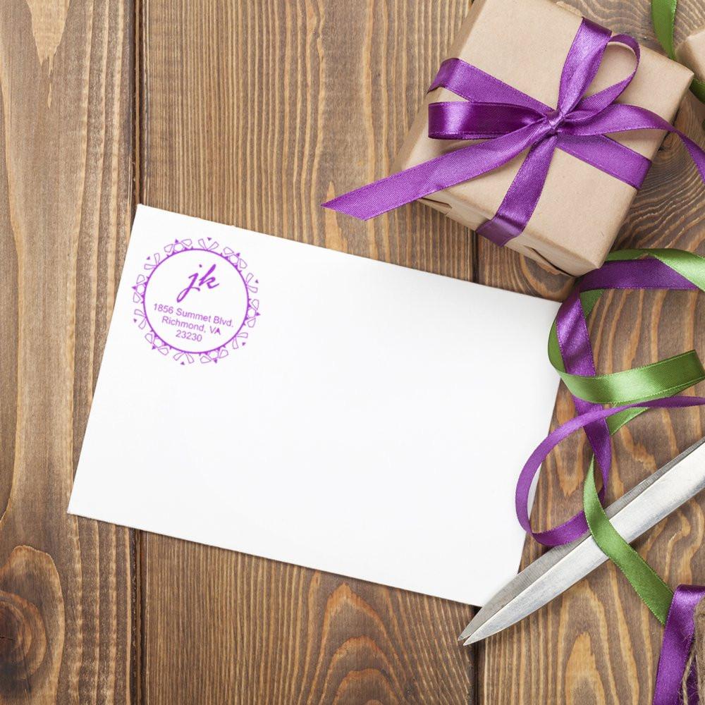 Custom return address rubber stamp on a white envelope with gift wrap, ribbons, and scissors on a rustic wood table.