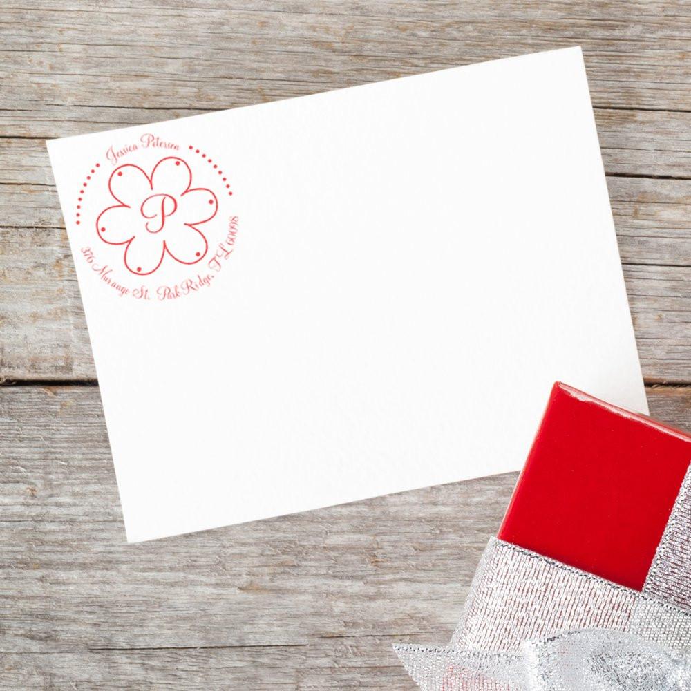 Custom return address rubber stamp with floral monogram on envelope, shown beside a red ink pad on rustic wood.