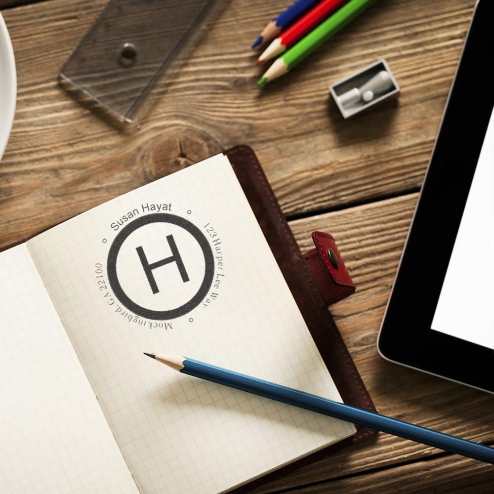 Notebook with Susan Hayat branding logo and pencil on wooden desk beside laptop, drafting personal identity details.