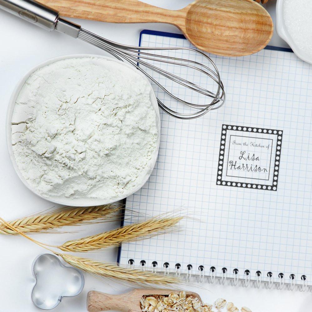 Personalized kitchen rubber stamp design on a recipe notebook with flour, whisk and baking tools for baking-themed branding.