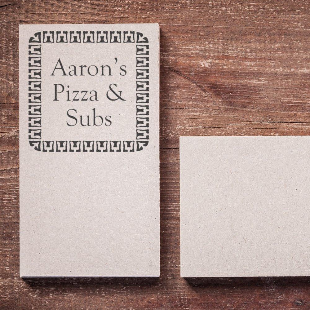 Custom rubber stamp for Aarons Pizza & Subs with decorative border, shown stamped on paper beside a blank card.