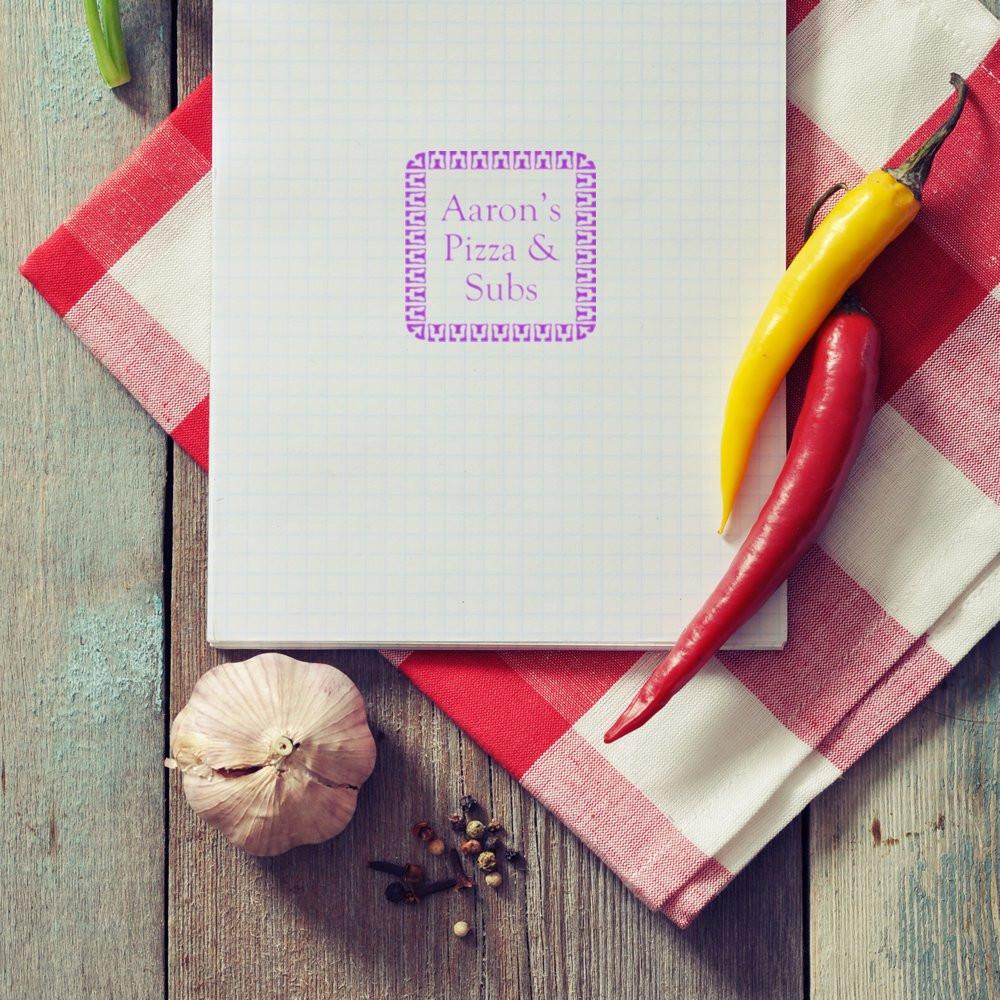Custom restaurant rubber stamp logo for Aarons Pizza & Subs, shown on notepad with peppers and garlic for branding.