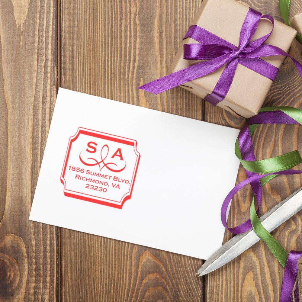 Custom return address rubber stamp on envelope beside gift wrap, ribbon, and scissors for personalized mailing.